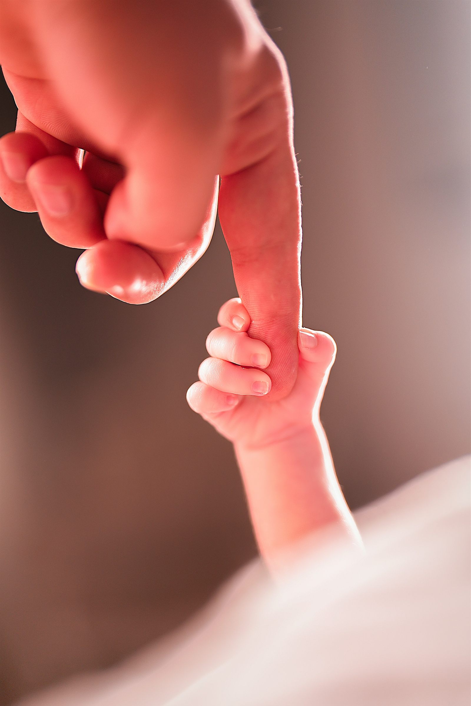 Main minuscule d'un nouveau-né serrant le doigt d'un parent, lumière douce et tons rosés, accompagnement périnatalité et FIV-PMA en sophrologie avec Anaïs Leneau, Rueil-Malmaison.